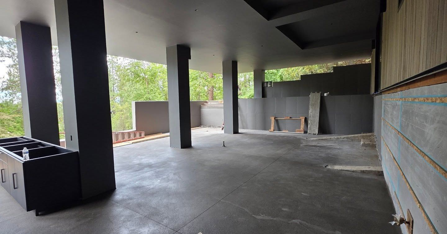 Empty covered patio with concrete floor, support columns, and a built-in grill on the left.