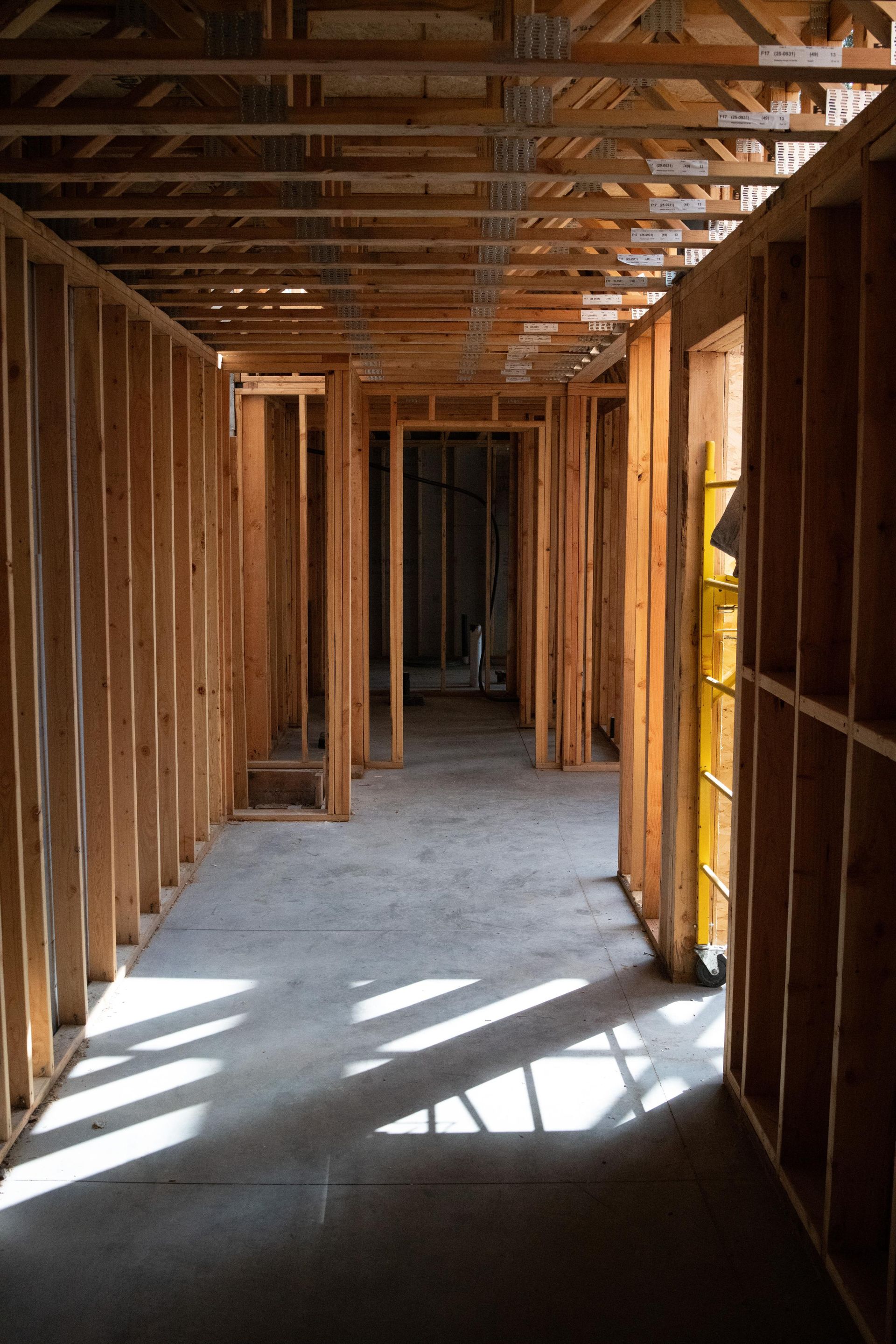 Interior of an unfinished wooden house with exposed framing and sunlight streaming through window openings