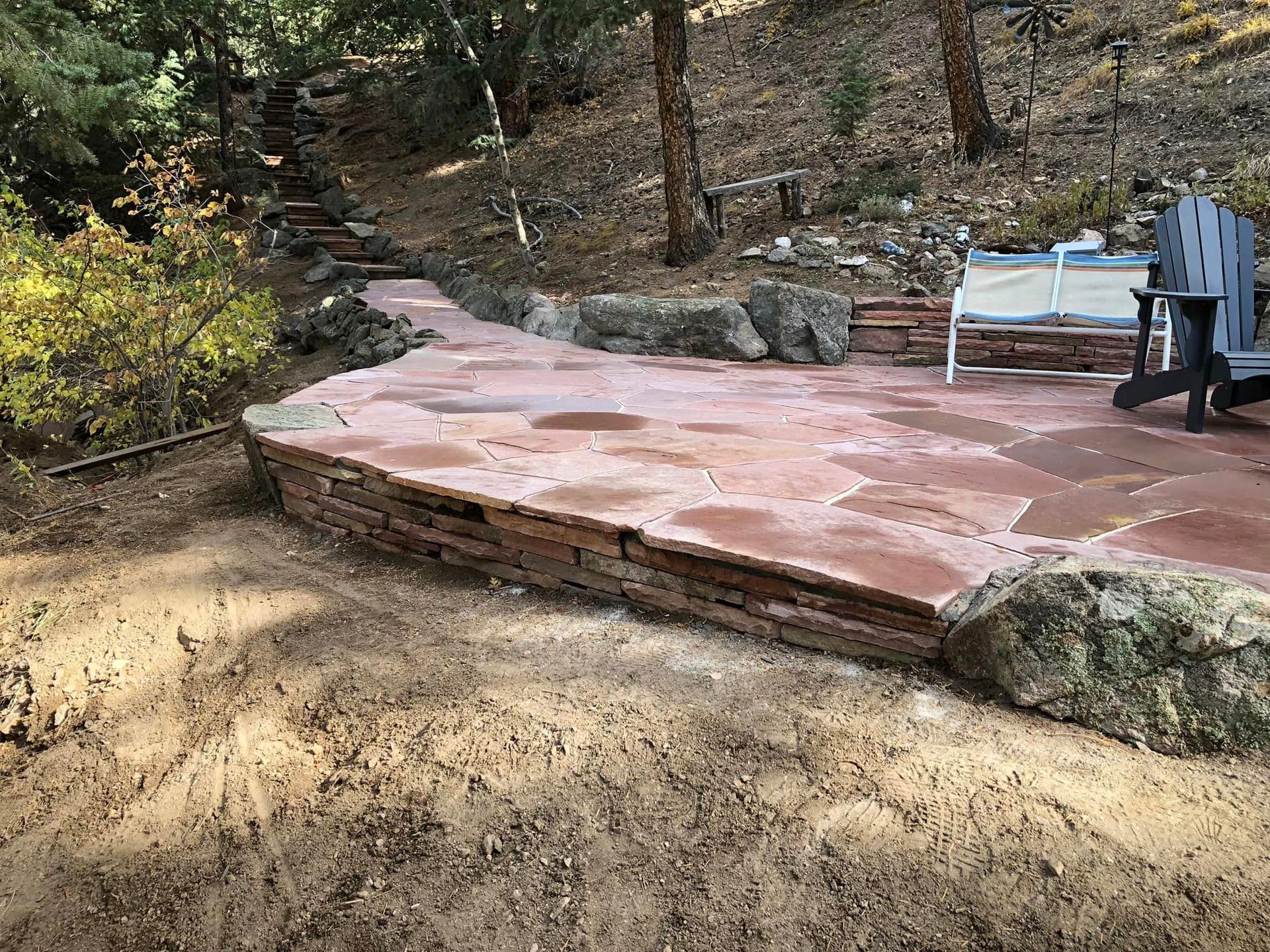 A patio with a chair and a bench in the woods.