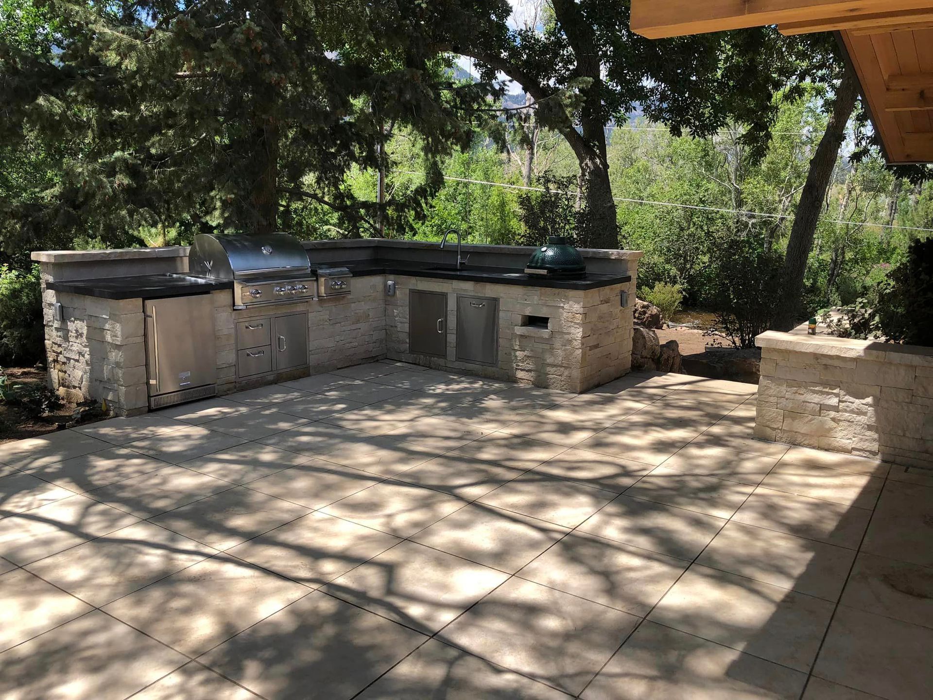 A large outdoor kitchen with a grill and a sink is surrounded by trees.