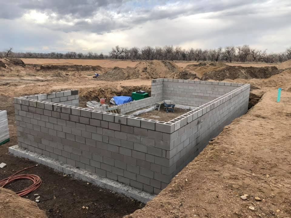 A large brick wall is being built in a dirt field.