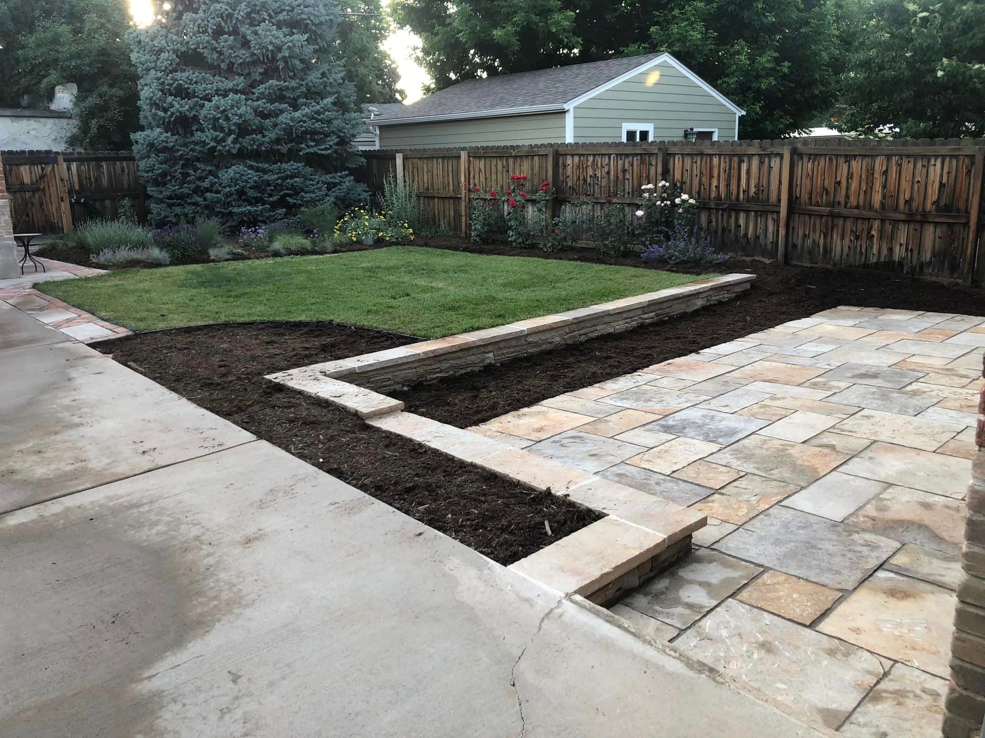 A backyard with a patio and a fence and a house in the background.