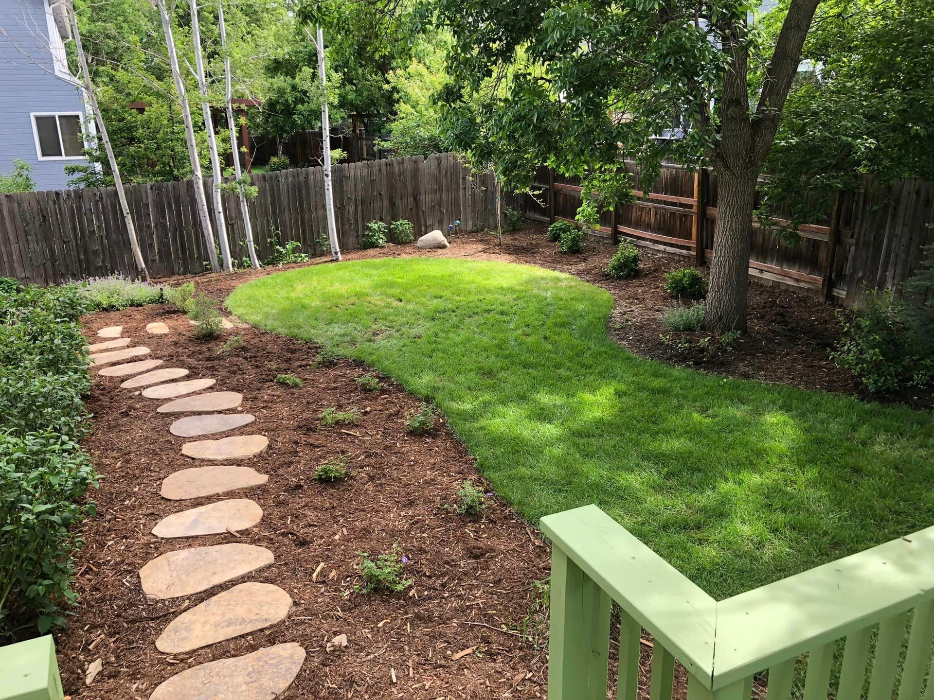 A backyard with a stone walkway leading to a lush green lawn.