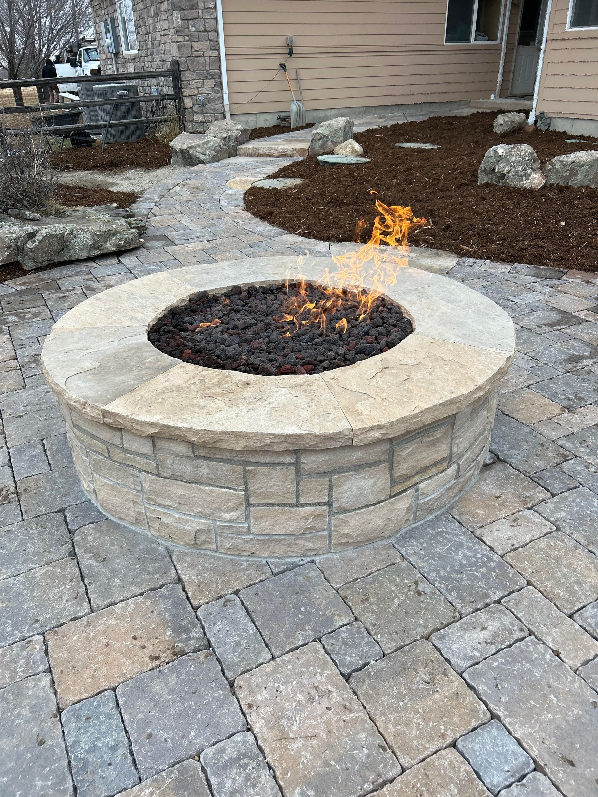 A fire pit is sitting on a brick patio in front of a house.