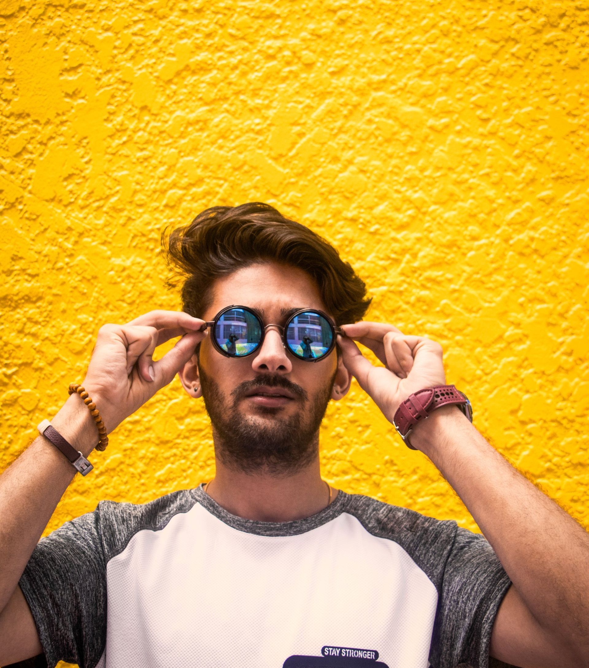 A man wearing sunglasses is standing in front of a yellow wall.