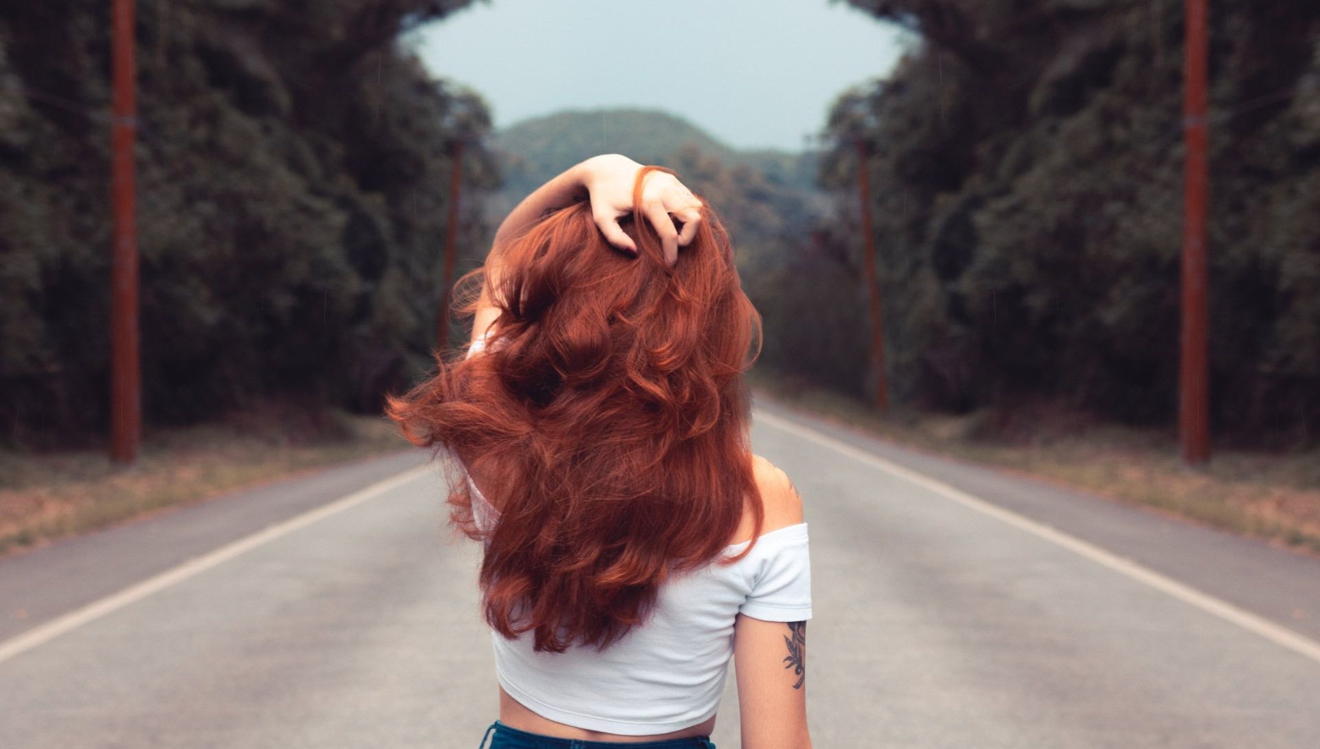 A woman with red hair is standing in the middle of a road.