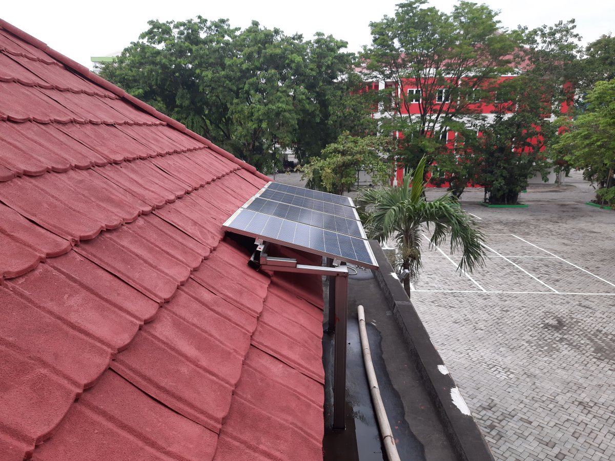 Solar panels mounted on a red tile roof overlooking a parking lot with green trees in the background.