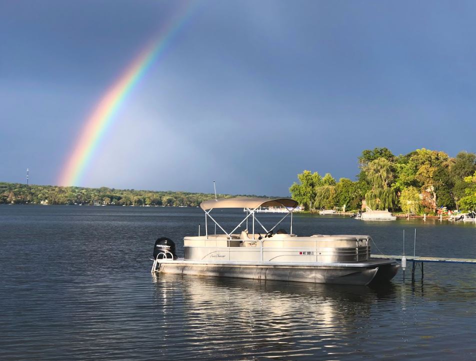 A pontoon boat is floating on a lake under a rainbow.