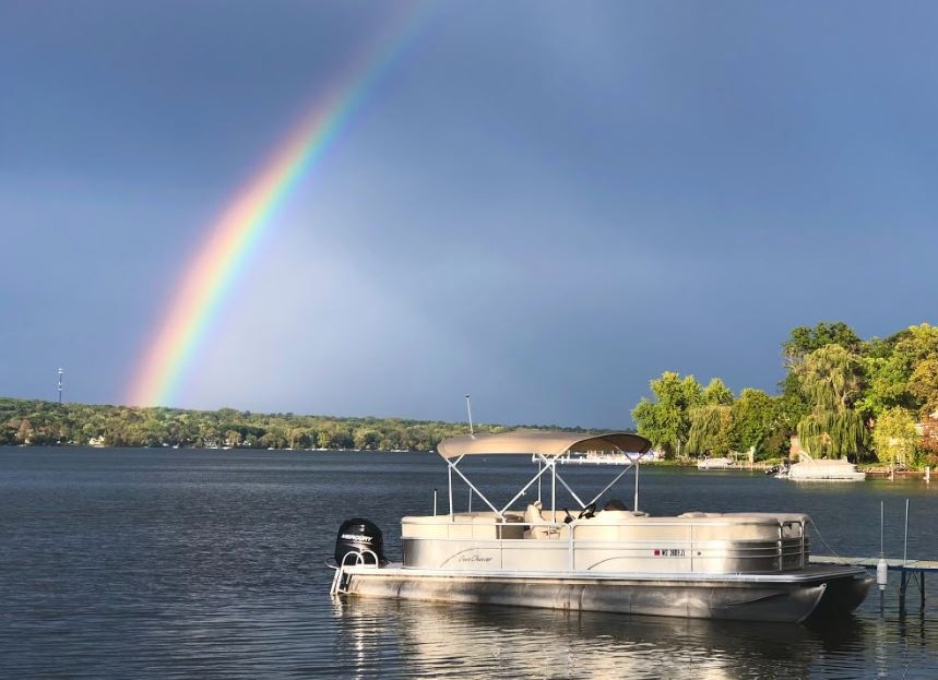 A pontoon boat is docked on a lake under a rainbow.