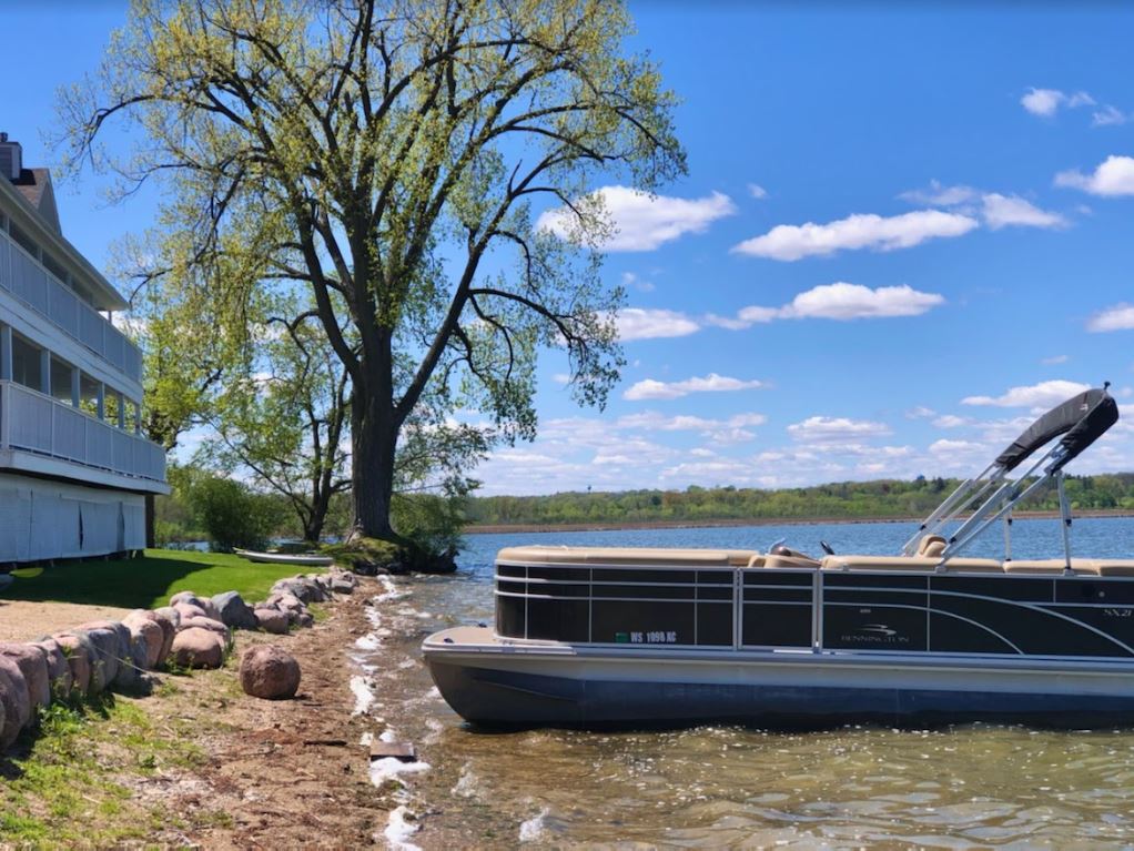 A pontoon boat is docked on the shore of a lake.