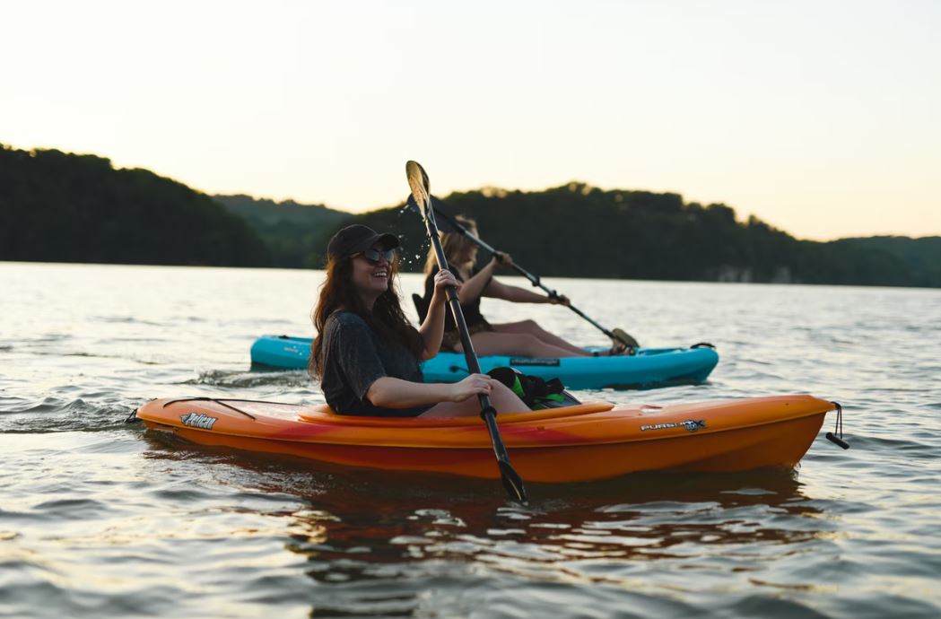 Two people are paddling kayaks on a lake.
