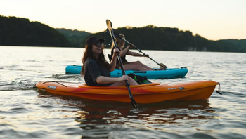 A man and a woman are paddling kayaks on a lake.