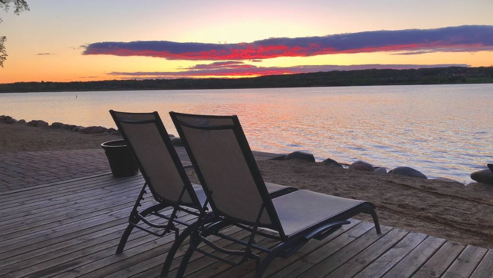 Two lounge chairs on a deck overlooking a lake at sunset