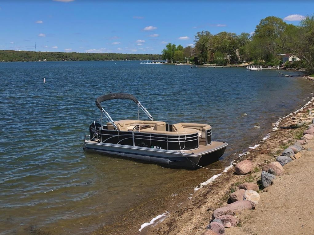 A pontoon boat is docked on the shore of a lake.