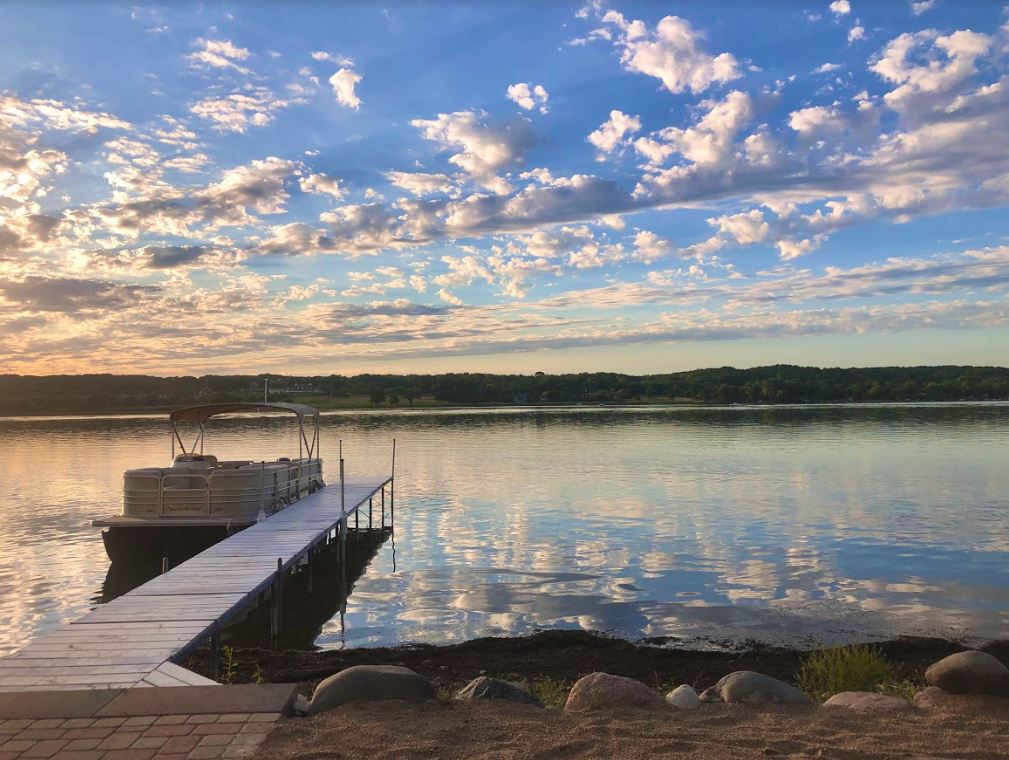 A boat is docked at a dock on a lake at sunset.