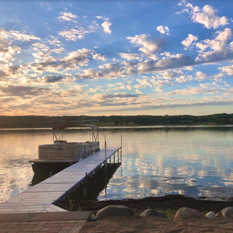 A boat is docked at a dock on a lake at sunset.