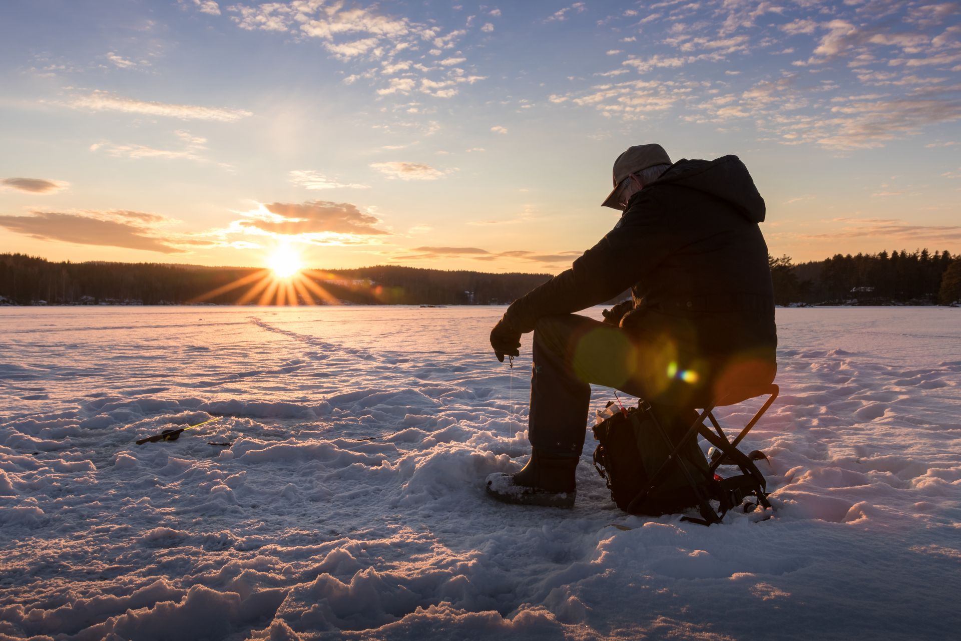 A man is sitting on a stool on a frozen lake at sunset.