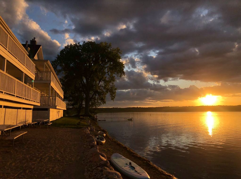A paddle board is sitting on the shore of a lake at sunset.