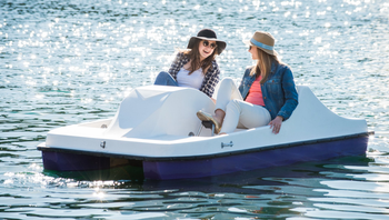 Two women are riding a pedal boat on a lake.