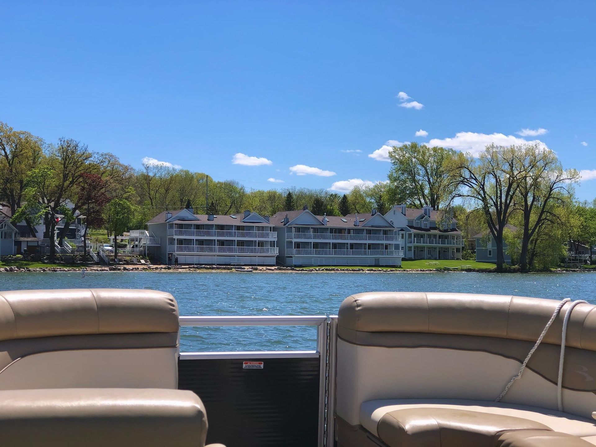 A pontoon boat is floating on a lake with houses in the background.