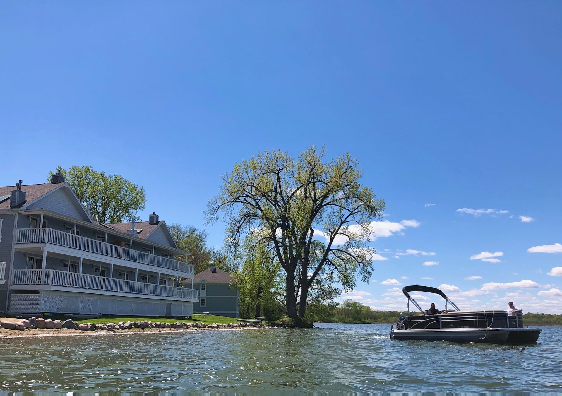 A boat is floating on a lake next to a building and a tree.