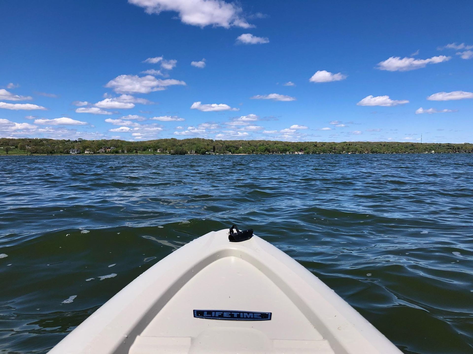 A white kayak is floating on a lake on a sunny day.