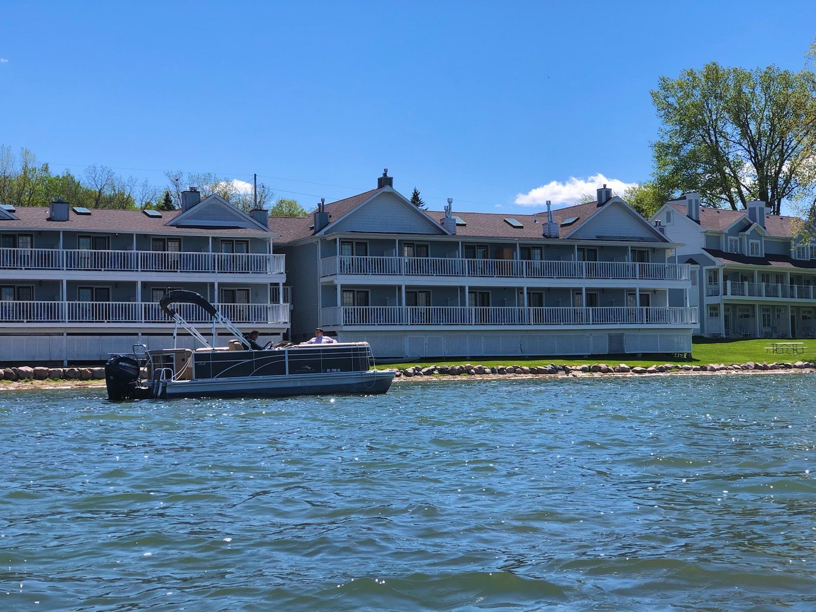A pontoon boat is floating on a lake in front of a building.