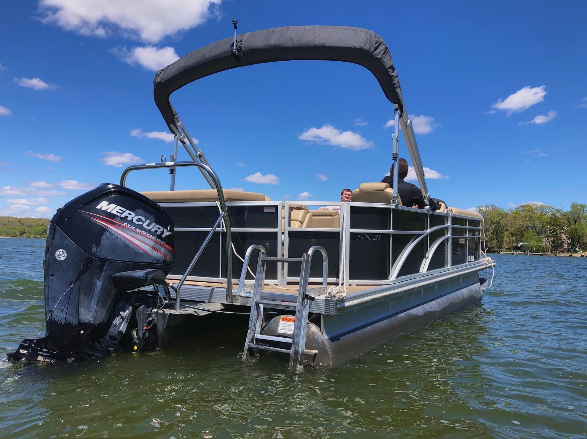 A pontoon boat with a mercury outboard motor is floating on a lake.