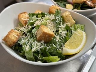 A close up of a caesar salad with croutons and a slice of lemon.