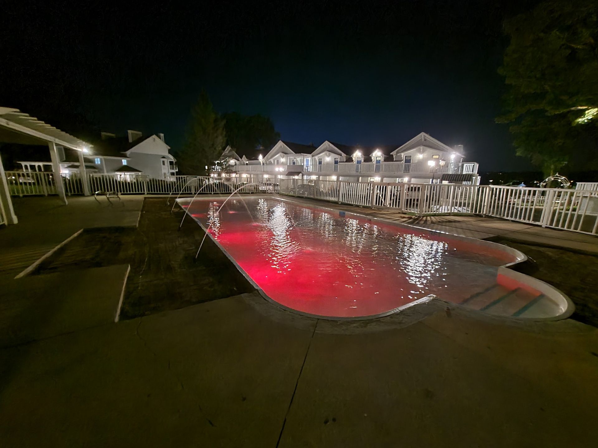 A large swimming pool is lit up at night with red lights.