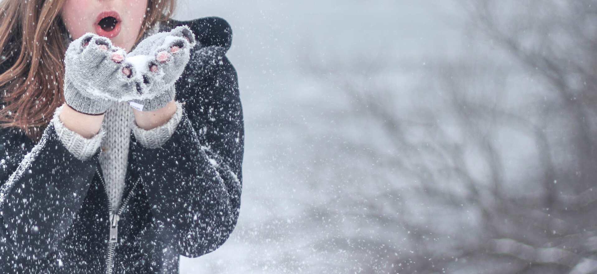 A woman is blowing snow from her hands in the snow.
