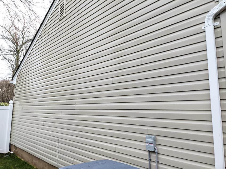 The side of a house with vinyl siding and a white fence.