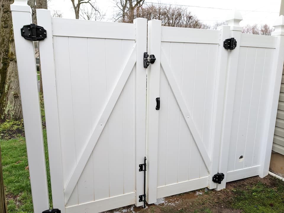 A white fence with a black gate is sitting in the grass.