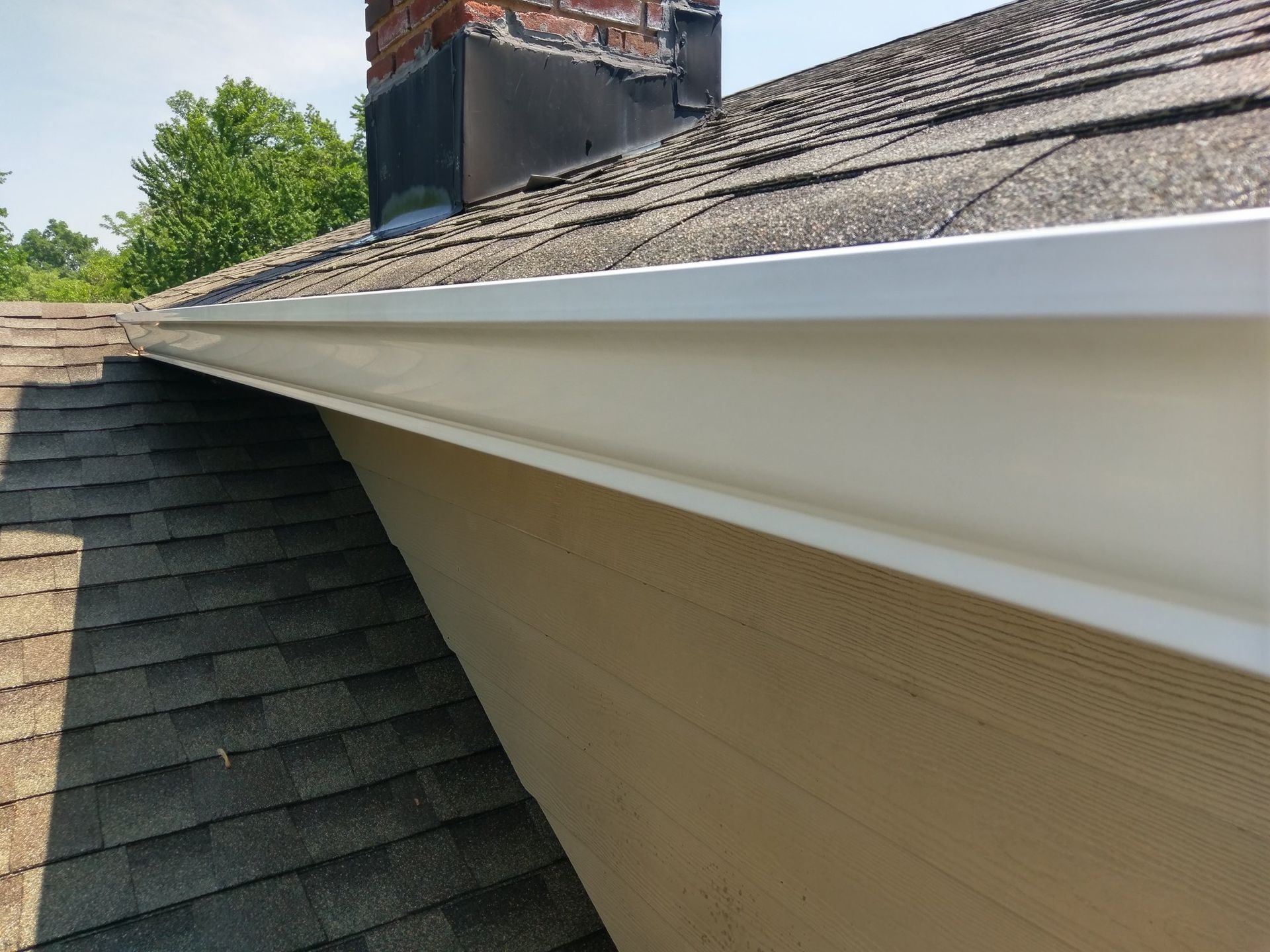 A white gutter is on the side of a house next to a roof.