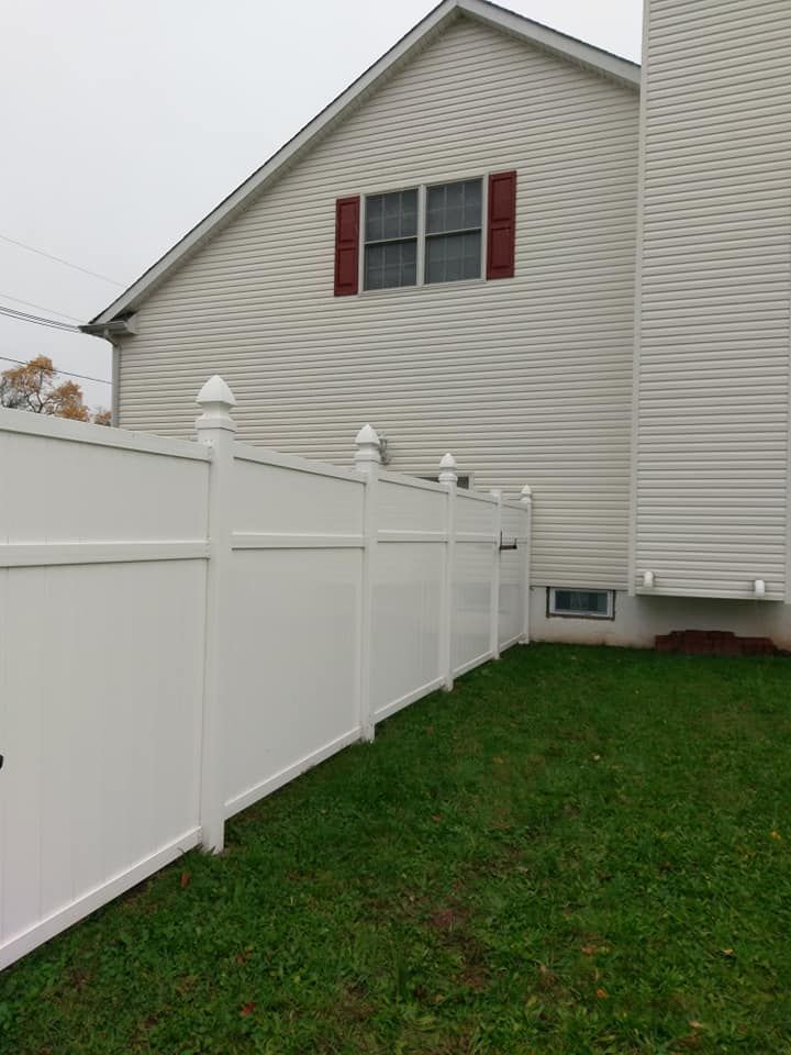 A white fence is in front of a house with red shutters.