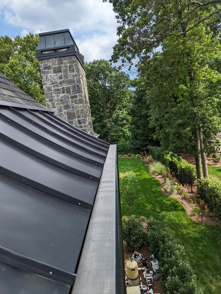 A roof with a gutter on it and a stone chimney in the background.