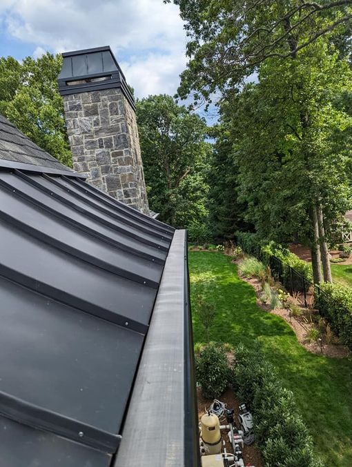 A roof with a gutter on it and a stone chimney in the background.