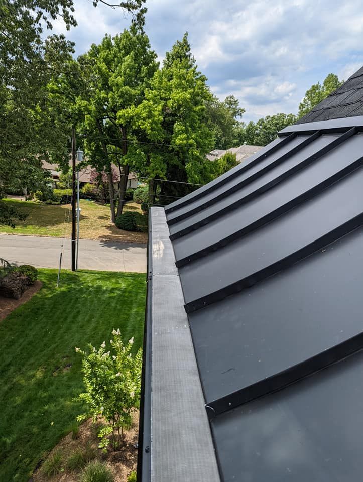 A close up of a gutter on a roof with trees in the background.