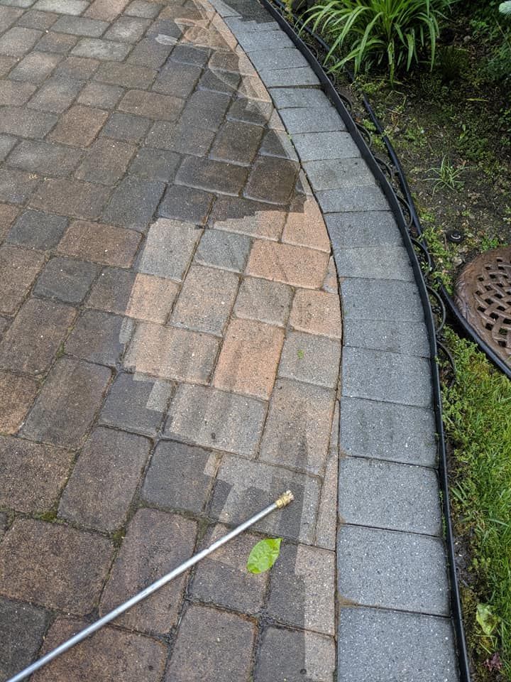 A person is cleaning a brick walkway with a sprayer.