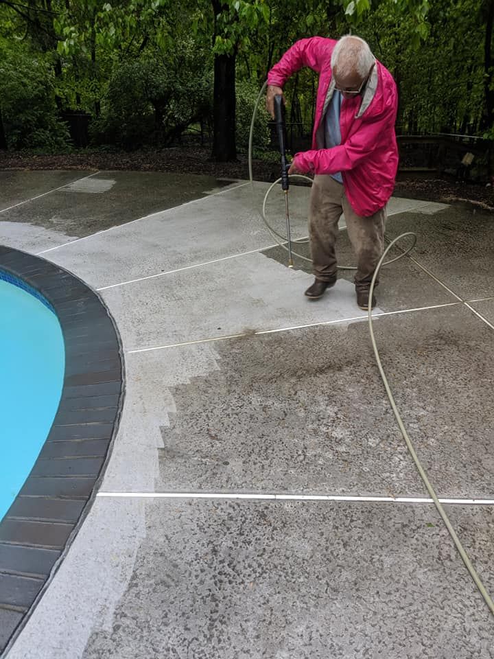 A man is cleaning a concrete patio next to a pool.