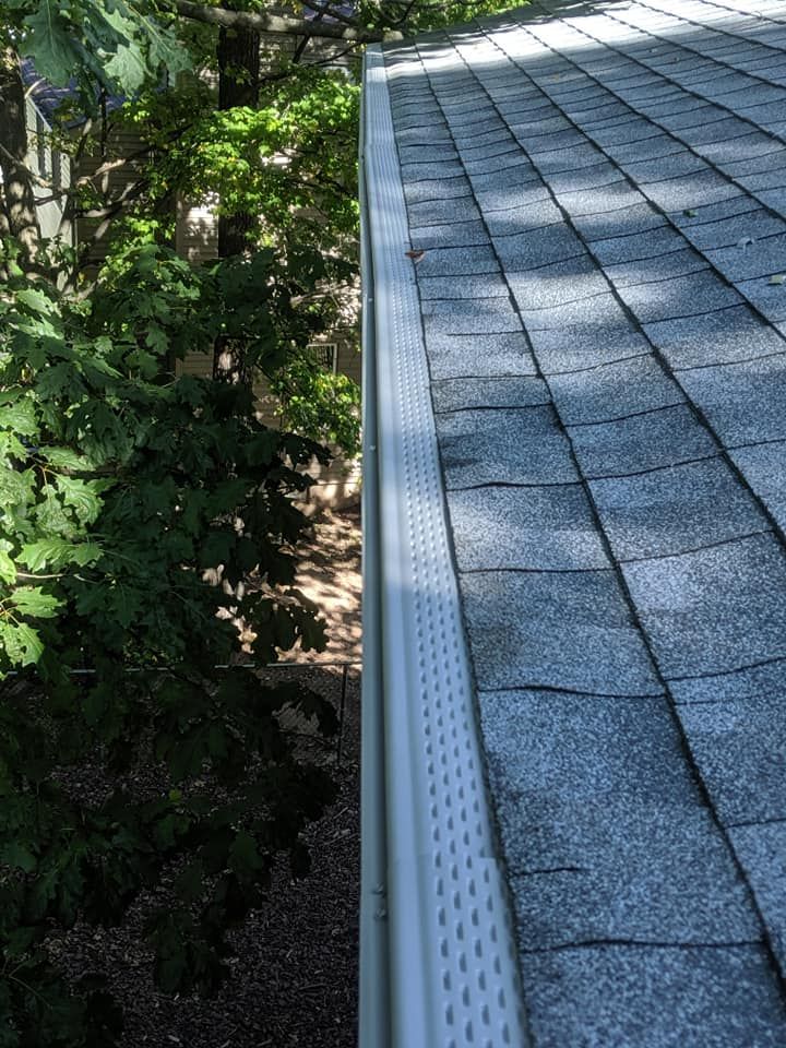 A close up of a gutter on a roof with trees in the background.
