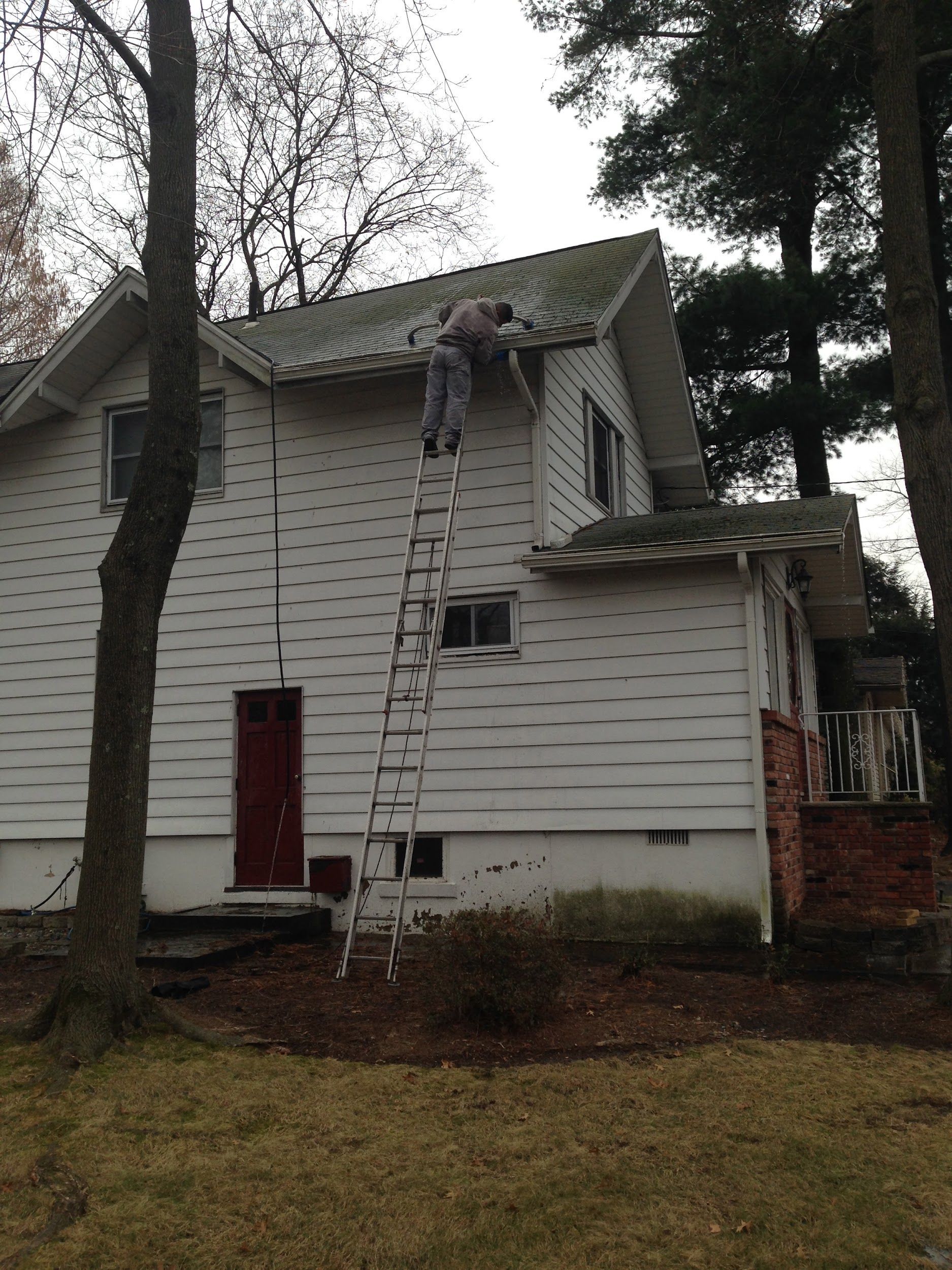 A man on a ladder paints the roof of a white house