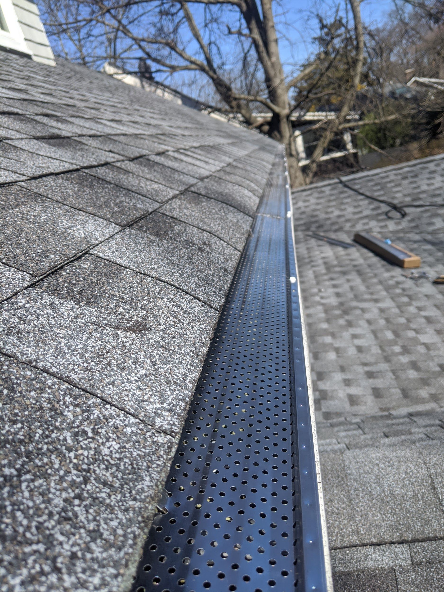A close up of a gutter on a roof with a tree in the background.