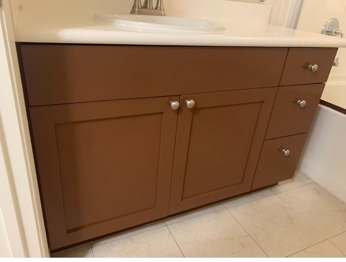 Brown bathroom vanity cabinet with silver knobs and a white countertop beside a sink