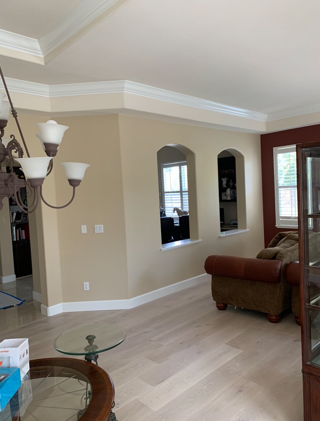 Bright living room with beige walls, white trim, arched mirrors, and a brown sofa near a window.