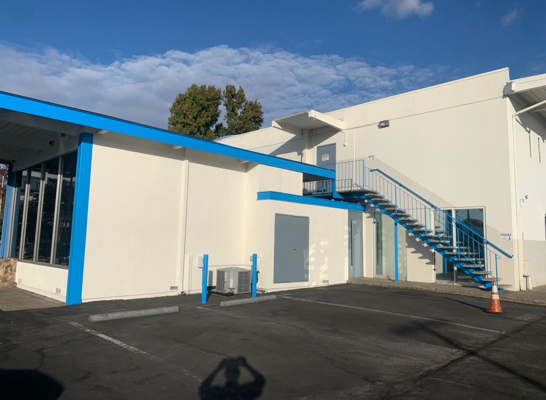 White building with blue trim and external staircase in a sunny parking lot
