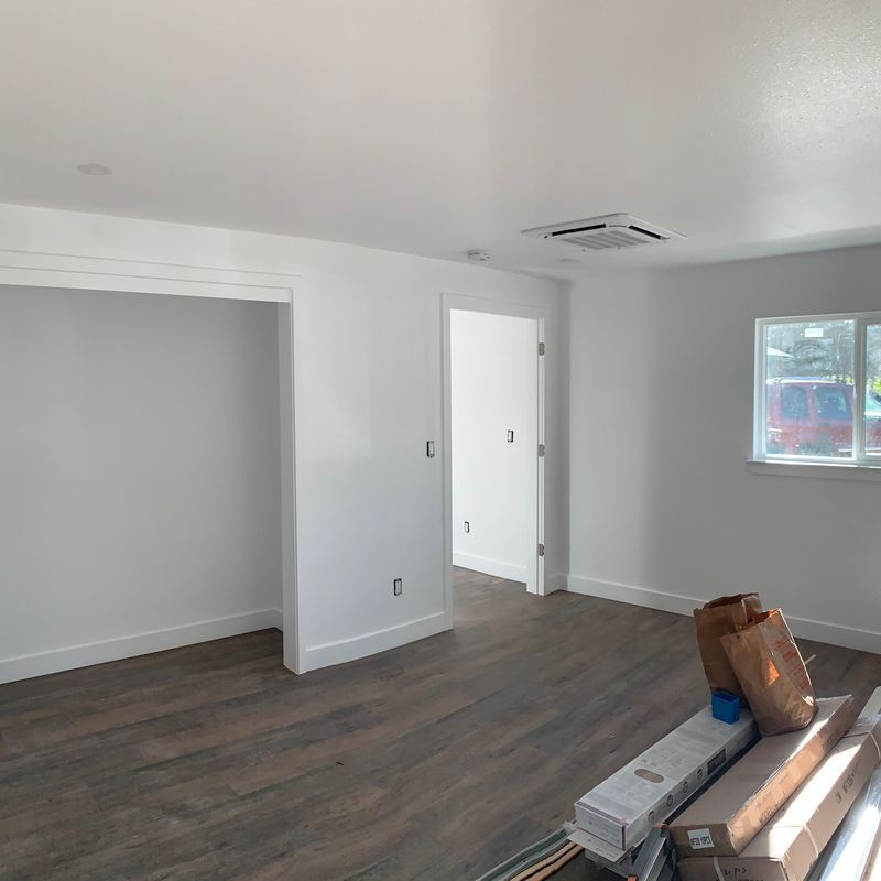 Empty gray room with wood flooring, a window, and construction materials stacked on the floor