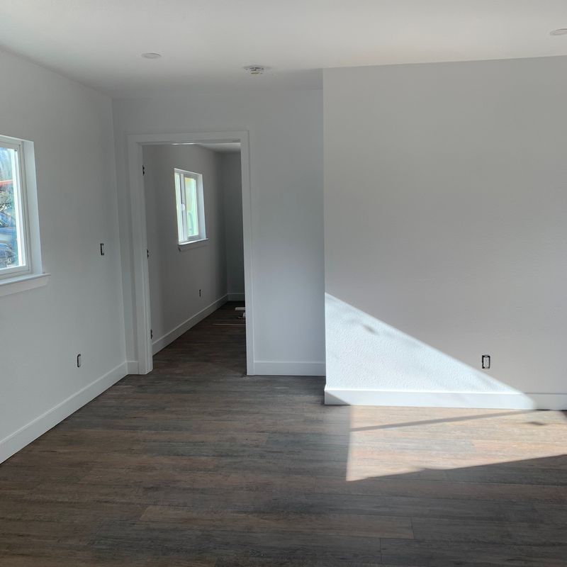 Bright empty room with white walls, dark wood floors, and sunlight casting a diagonal shadow.