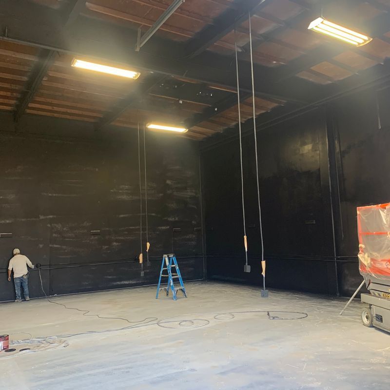 Empty warehouse interior with a worker, blue ladder, hanging lights, and construction materials on the floor