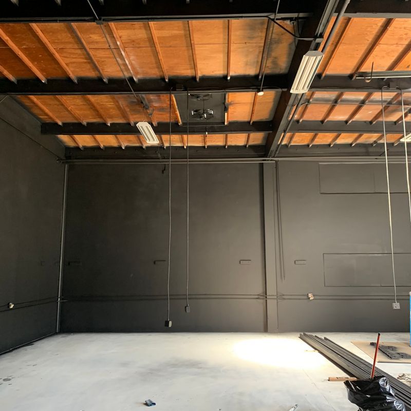 Empty industrial room with black walls, exposed wood ceiling beams, and a concrete floor under construction